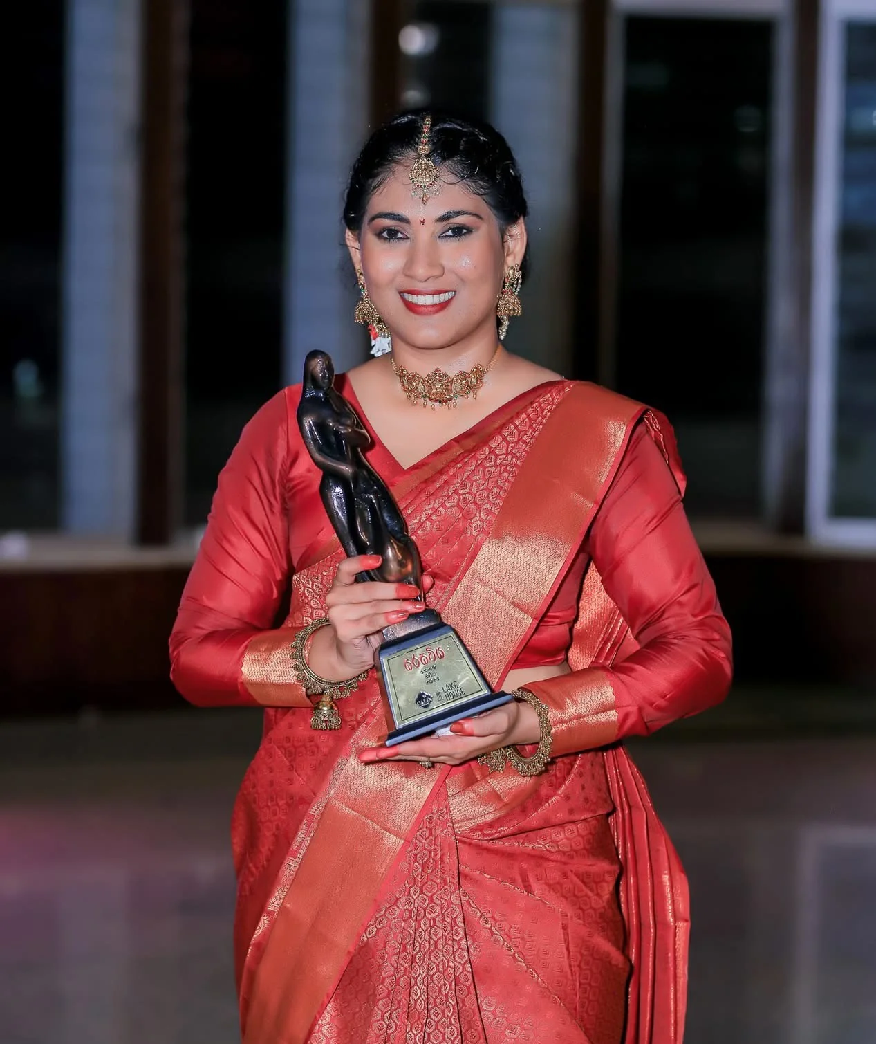 Thilakshini Ratnayake holding the Sarasaviya Best Actress Statuette in red silk sari